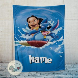 May include: Blue blanket featuring Stitch and Lilo surfing a wave. The blanket has a blue background with the word "Name" in white block letters. The blanket is displayed against a gray wall.