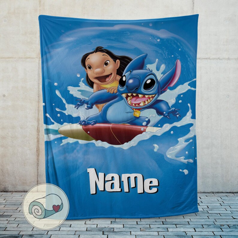May include: Blue blanket featuring Stitch and Lilo surfing a wave. The blanket has a blue background with the word "Name" in white block letters. The blanket is displayed against a gray wall.
