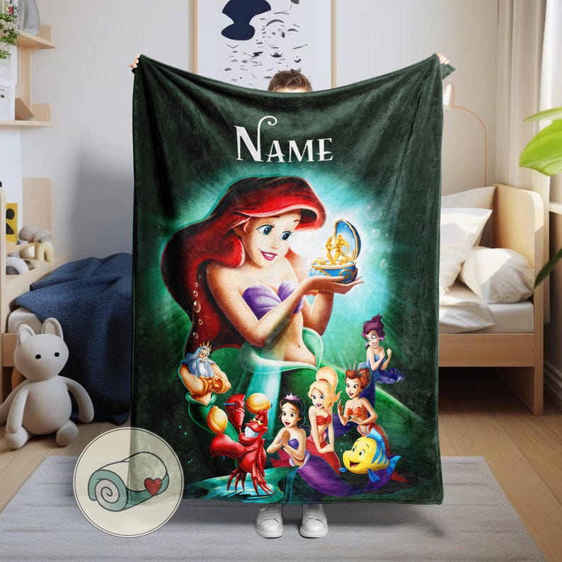 May include: A dark green plush blanket featuring a colorful illustration of Ariel from The Little Mermaid. The design includes Ariel, Flounder, Sebastian, and other characters. The word "Name" is written in white script at the top.