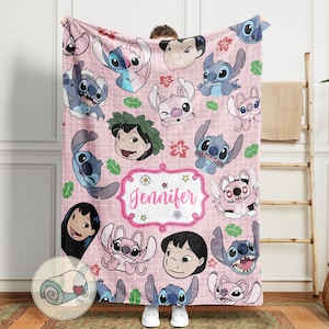 May include: A pink blanket featuring cartoon characters and the name "Jennifer" in a decorative frame. The blanket has a grid pattern and includes images of Stitch and Lilo.