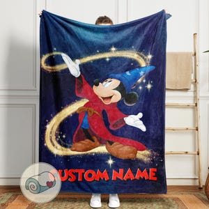 Op de afbeelding: Een marineblauwe fleece deken met een cartoonafbeelding van Mickey Mouse verkleed als tovenaar. Het ontwerp omvat een blauwe tovenaars hoed, rode mantel en de tekst "CUSTOM NAME" in het rood. Gouden glitters en een wervelend ontwerp maken het magische thema compleet.