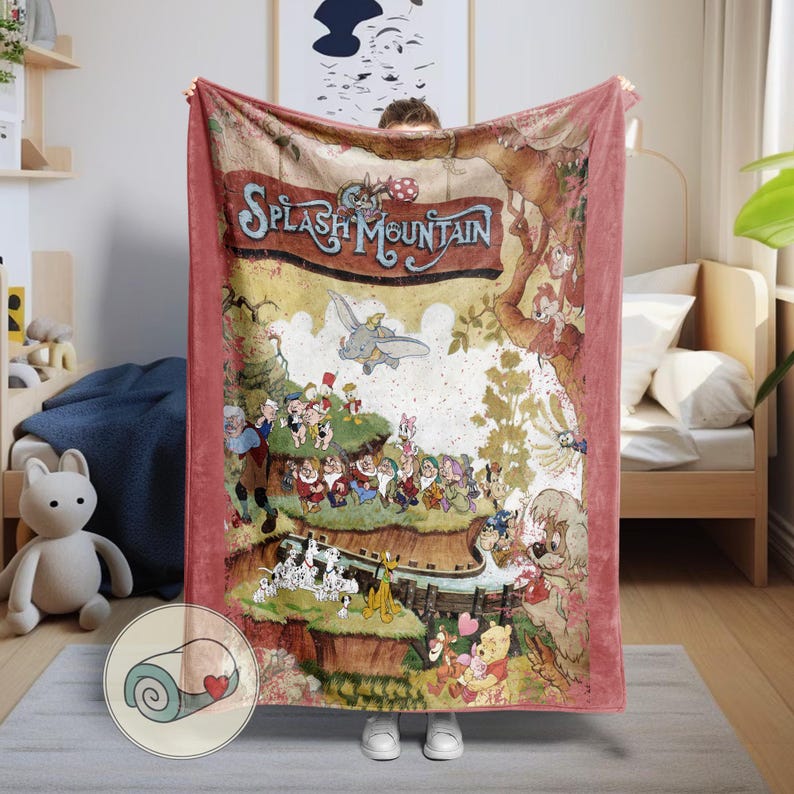 May include: A plush, pink blanket featuring a colorful illustration of characters from Splash Mountain. The design includes Dumbo, the Seven Dwarfs, and other Disney characters. The blanket is rolled up in a small circle with a heart.