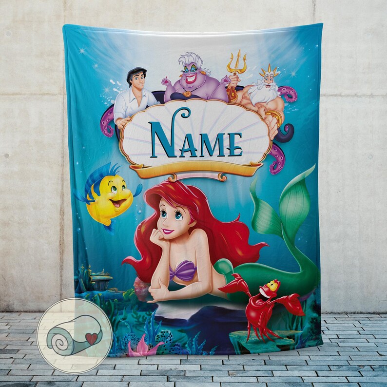 May include: A teal blanket featuring Ariel from The Little Mermaid, with other characters like Flounder, Sebastian, and Prince Eric. The blanket has a personalized name banner and a light blue background.