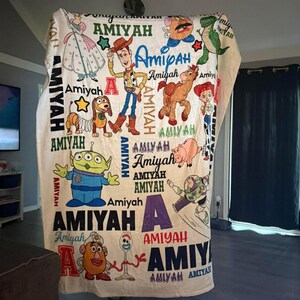 Pu&ograve; includere: Una coperta color crema con vari personaggi di Toy Story e il nome "Amiyah" in diversi stili. La coperta presenta illustrazioni di Woody, Buzz Lightyear e altri personaggi del film d'animazione.