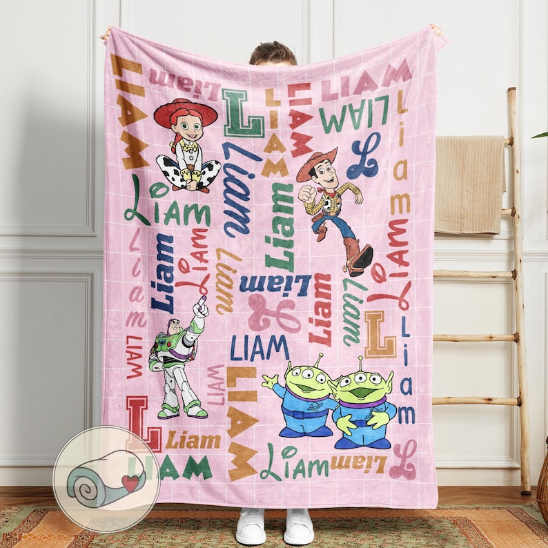 May include: Pink blanket featuring characters from the Toy Story movie, including Jessie, Woody, Buzz Lightyear, and the Little Green Men. The name "Liam" is printed in various fonts across the blanket. The blanket is a soft, cozy item.