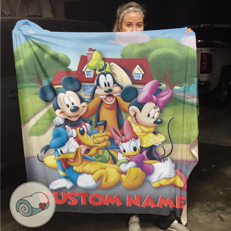 K&ouml;nnte beinhalten: Eine gro&szlig;e, rechteckige Decke mit einer farbenfrohen Illustration von Micky Maus, Minnie Maus, Goofy, Donald Duck, Daisy Duck und Pluto. Die Decke hat einen individuellen Namen, der unten in Rot aufgedruckt ist. Der Hintergrund zeigt ein Haus und eine Stra&szlig;e.