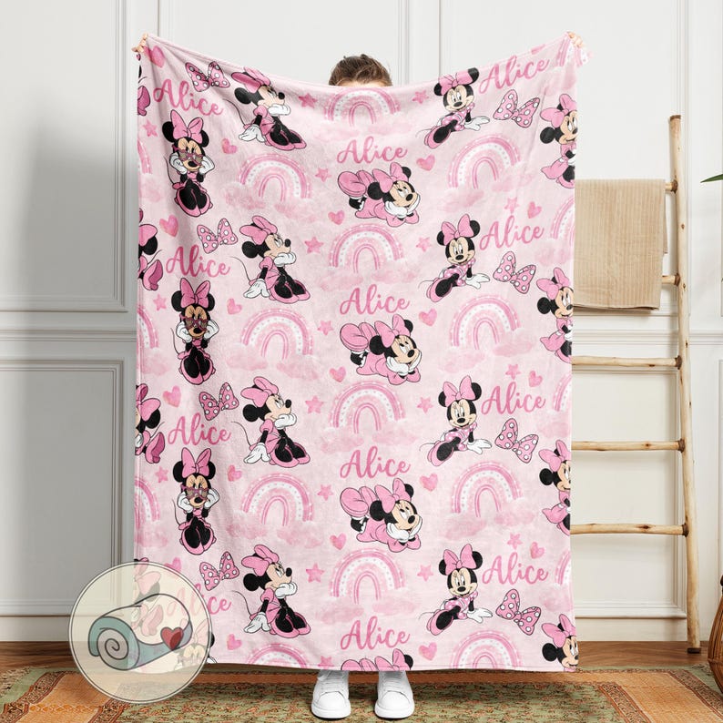 K&ouml;nnte beinhalten: Rosa Decke mit einem sich wiederholenden Muster von Minnie Mouse, Regenbogen, Herzen und dem Namen "Alice". Die Decke hat eine weiche Textur und ist f&uuml;r Komfort und W&auml;rme konzipiert.
