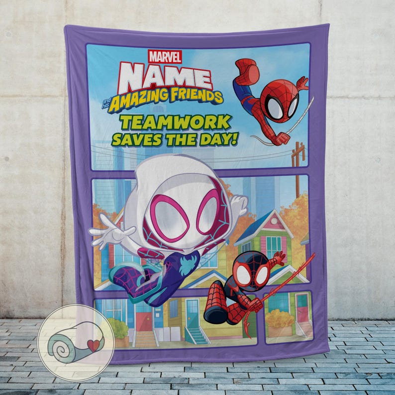 Op de afbeelding: Een paarse Marvel Amazing Friends deken met Spider-Man, Spider-Gwen en Miles Morales. De deken heeft de tekst "Teamwork Saves the Day!" en een cartoon stadsgezicht achtergrond.