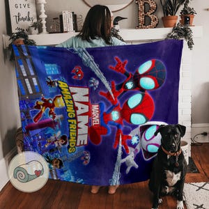 May include: A plush, blue blanket featuring Spider-Man and other Marvel characters. The blanket has the words "Amazing Friends" and "Marvel" printed on it. The design includes a cityscape background and various action poses.