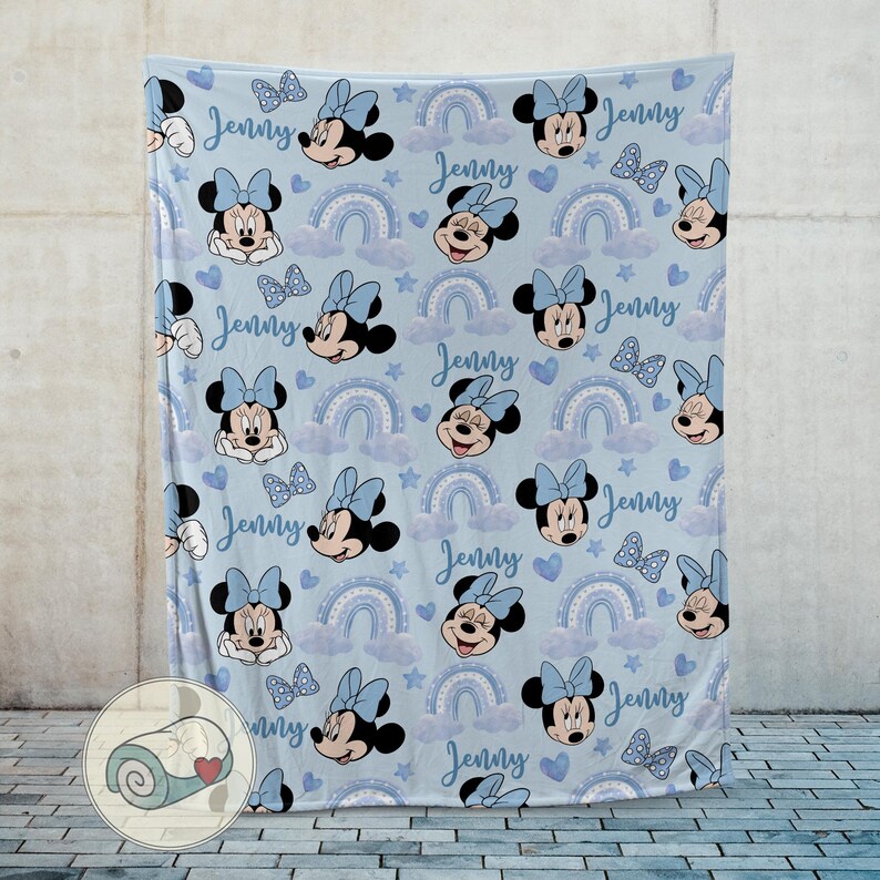 Puede incluir: Una manta azul claro con un estampado de Minnie Mouse, lazos, arco&iacute;ris y corazones. El nombre "Jenny" est&aacute; escrito en el dise&ntilde;o. Una manta suave y acogedora.