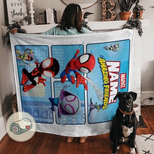 May include: A white blanket featuring a Marvel "Amazing Friends" design with Spider-Man and other characters. The blanket has a blue background with the Marvel logo and the word "NAME" in large letters.