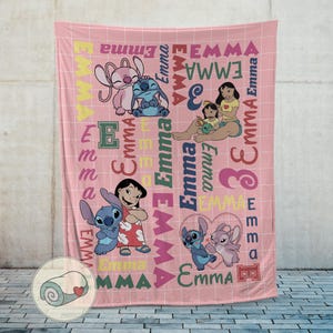 May include: Pink blanket featuring cartoon characters and the name "Emma" in various fonts and colors. The blanket has a grid pattern and includes images of Stitch and Angel. A rolled-up blanket with a heart is in the corner.