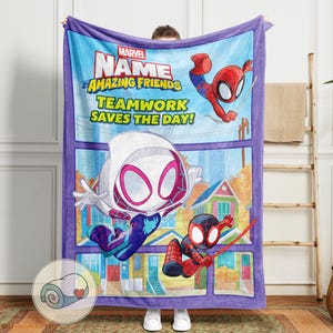 Op de afbeelding: Een rechthoekige, pluche deken met een paarse rand en een blauwe achtergrond, met Marvel's Spider-Man-personages. De deken heeft illustraties van Spider-Man, Spider-Gwen en Miles Morales. De tekst luidt "Marvel Amazing Friends Teamwork Saves the Day!"