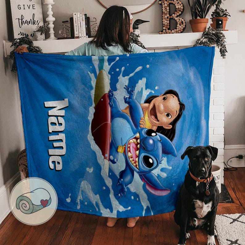 May include: A blue blanket featuring Stitch and Lilo from the Disney movie. The blanket has a wave design and the word "Name" in white. A black dog with a brown collar sits in front of the blanket.