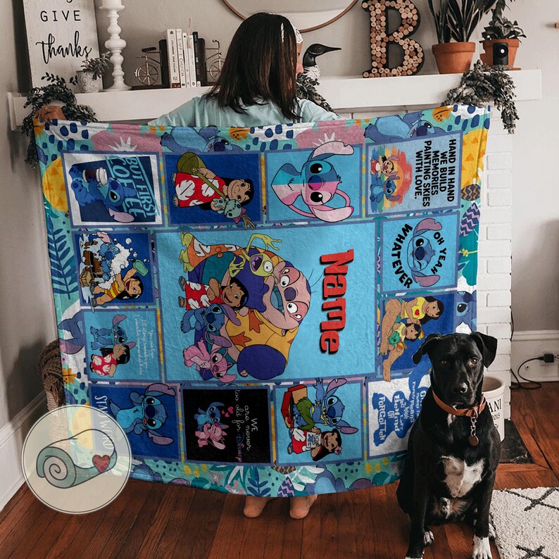 May include: A blue blanket featuring cartoon characters, including Stitch, with the name "Name" in red. The blanket has various rectangular panels with character illustrations and text. A black dog with a brown collar sits in front of the blanket.