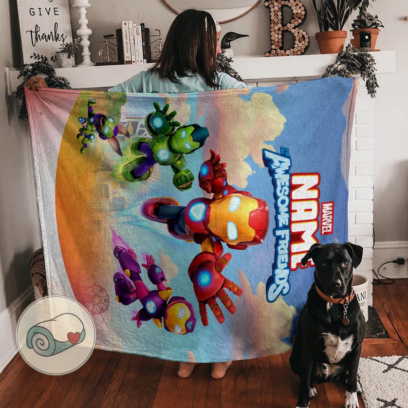 K&ouml;nnte beinhalten: Eine Marvel "Awesome Friends" Decke mit Iron Man und anderen Charakteren in einem farbenfrohen Design. Die Decke hat einen blauen Hintergrund mit dem Marvel-Logo und dem Wort "NAME" darauf. Ein schwarzer Hund sitzt auf dem Boden.