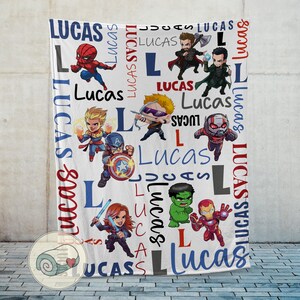 Puede incluir: Manta blanca con superh&eacute;roes de dibujos animados y el nombre "Lucas" en azul y rojo. El dise&ntilde;o incluye personajes como Spider-Man, Capit&aacute;n Am&eacute;rica e Iron Man. La palabra "Lucas" se repite.