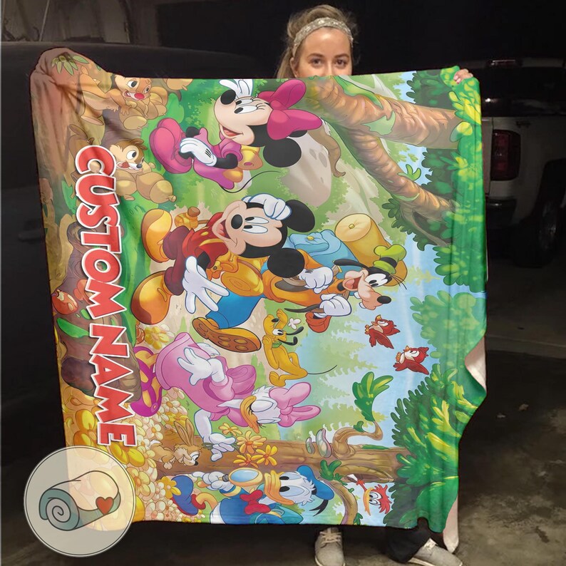 May include: A colorful blanket featuring Mickey Mouse, Minnie Mouse, Goofy, Donald Duck, and other cartoon characters in a forest setting. The blanket has the words "CUSTOM NAME" printed vertically in red. The blanket is held up by a person.