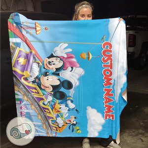 May include: A blue blanket featuring Mickey Mouse, Minnie Mouse, and Donald Duck on a roller coaster. The blanket has a blue sky background with white clouds and the text "CUSTOM NAME" in red.