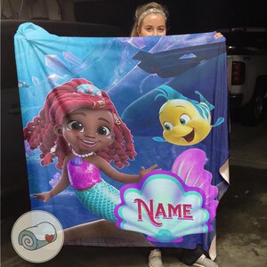 Peut inclure: Une couverture color&eacute;e repr&eacute;sentant une sir&egrave;ne de dessin anim&eacute; aux cheveux roux, un haut rose et une queue turquoise. Un poisson jaune est &eacute;galement repr&eacute;sent&eacute;. La couverture a un fond bleu avec le mot "Name" dans un cadre en forme de coquillage.
