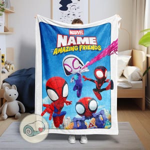 May include: A large, rectangular Marvel blanket featuring Spider-Man and his Amazing Friends. The blanket has a blue background with the Marvel logo and the words "NAME" and "Amazing Friends" in white and yellow. The blanket is white around the edges.