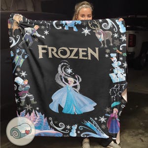 Op de afbeelding: Zwarte deken met personages en afbeeldingen uit de film "Frozen". De deken heeft Elsa in het midden, omringd door sneeuwvlokken, en andere personages zoals Olaf, Anna en Kristoff. Het woord "FROZEN" staat in grote letters afgebeeld.