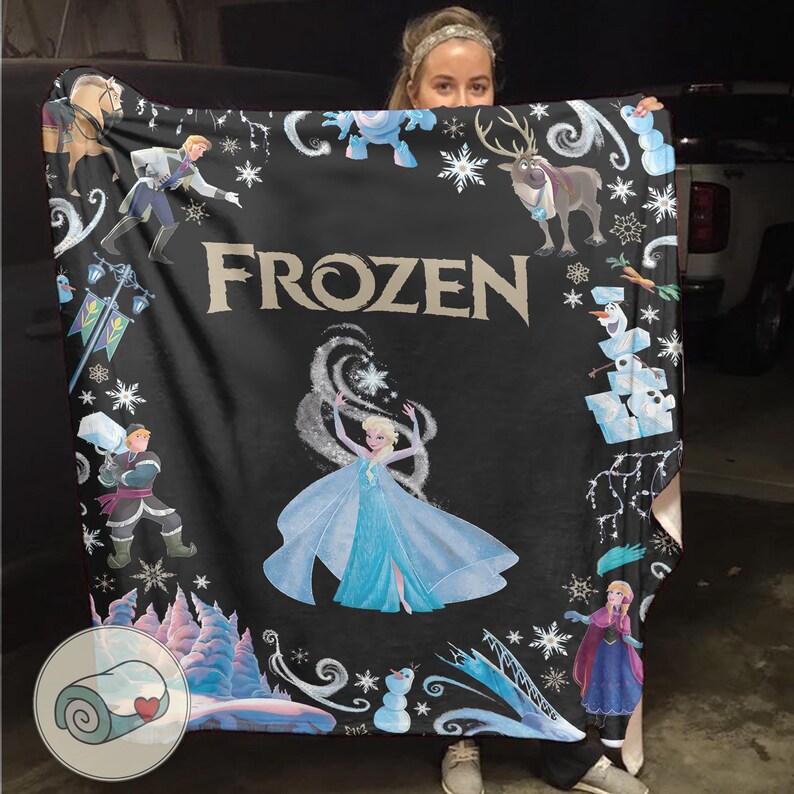 Op de afbeelding: Zwarte deken met personages en afbeeldingen uit de film "Frozen". De deken heeft Elsa in het midden, omringd door sneeuwvlokken, en andere personages zoals Olaf, Anna en Kristoff. Het woord "FROZEN" staat in grote letters afgebeeld.