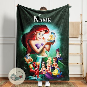 May include: A dark green fleece blanket featuring a colorful illustration of Ariel from The Little Mermaid. The blanket has the word "Name" in white script at the top. The image includes Ariel, King Triton, Sebastian, Flounder, and other mermaids.