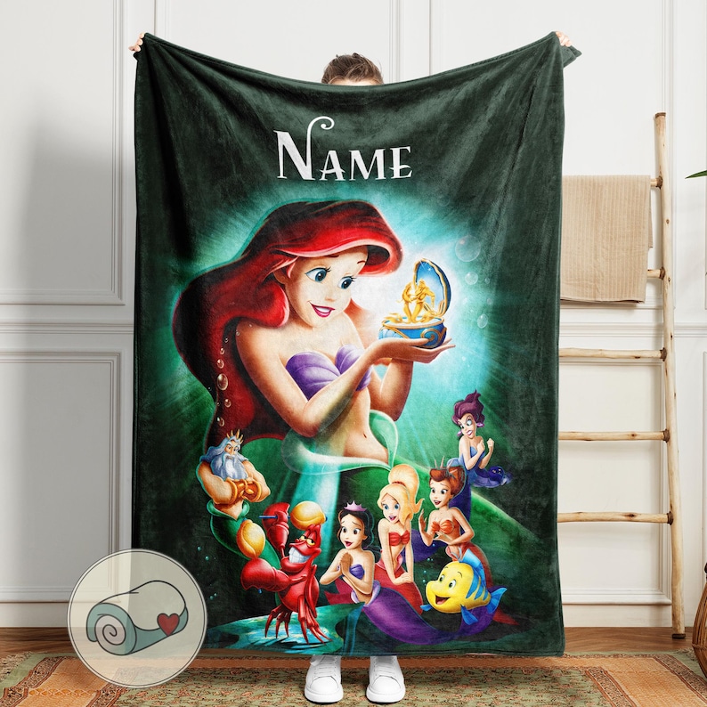 May include: A dark green fleece blanket featuring a colorful illustration of Ariel from The Little Mermaid. The blanket has the word "Name" in white script at the top. The image includes Ariel, King Triton, Sebastian, Flounder, and other mermaids.