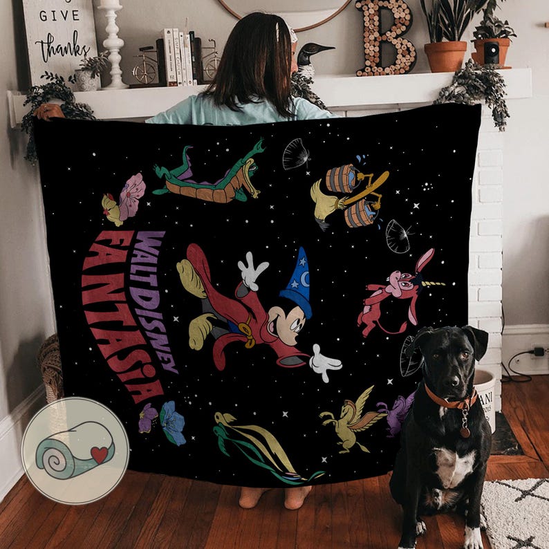 May include: Black blanket with a Walt Disney Fantasia design, featuring Mickey Mouse and other characters. The blanket has the words "Fantasia" and "Walt Disney" printed on it. A black dog with a red collar is sitting on the floor.