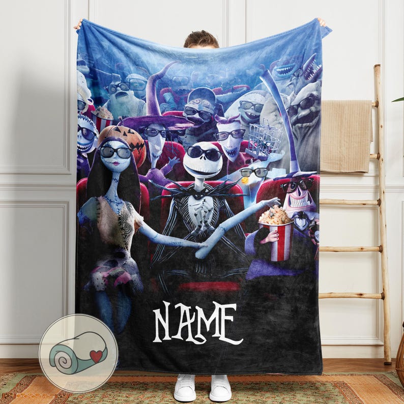 Puede incluir: Una manta de felpa con una escena de Pesadilla antes de Navidad. Jack Skellington y Sally est&aacute;n en un cine con otros personajes. La manta es principalmente negra, azul y roja, con la palabra "NAME" en blanco.