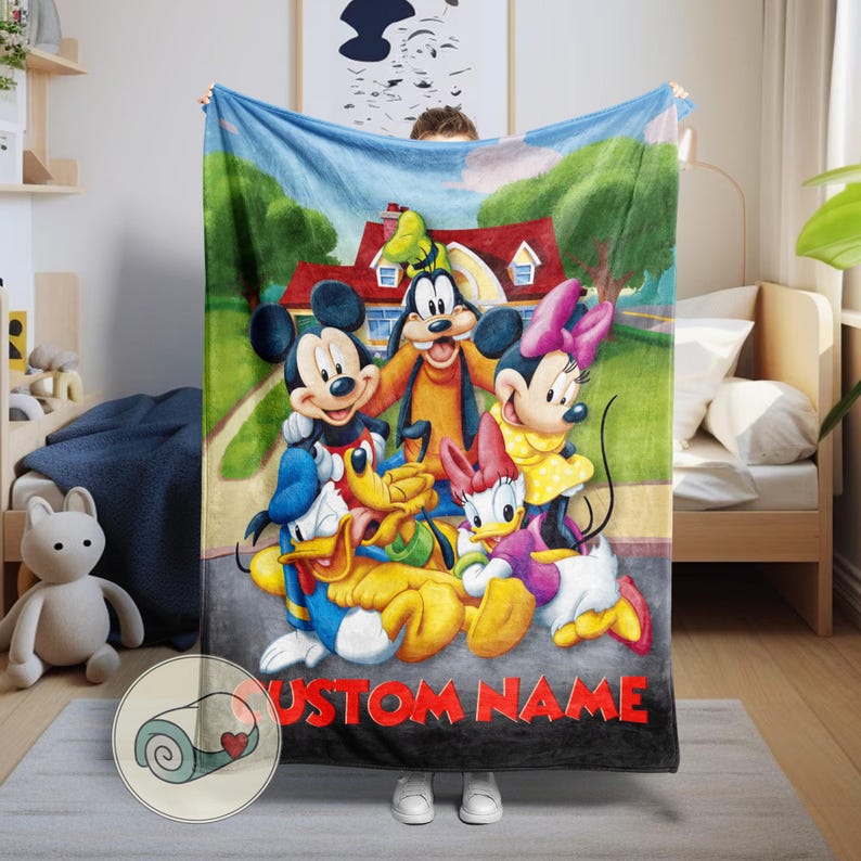 K&ouml;nnte beinhalten: Eine weiche Decke mit Mickey Mouse, Minnie Mouse, Goofy, Donald Duck und Daisy Duck in einer farbenfrohen Cartoon-Szene. Die Decke hat einen blauen Himmel als Hintergrund mit einem Haus und dem Text "CUSTOM NAME" in Rot.