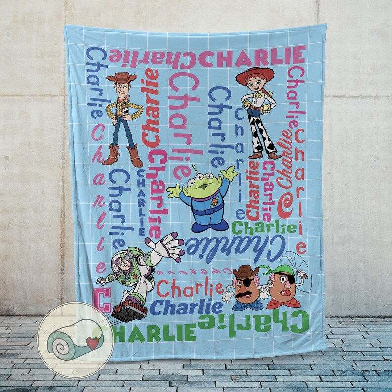 May include: A light blue blanket featuring cartoon characters and the name "Charlie" in various colors and fonts. The blanket showcases characters like Woody, Jessie, Buzz Lightyear, and others from a popular animated movie.
