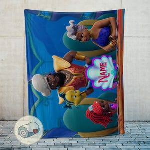 May include: A blue fleece blanket with cartoon characters from a popular animated movie. The blanket features a mermaid, a sea creature, and a man in a red and gold outfit. The word "NAME" is visible on the blanket.