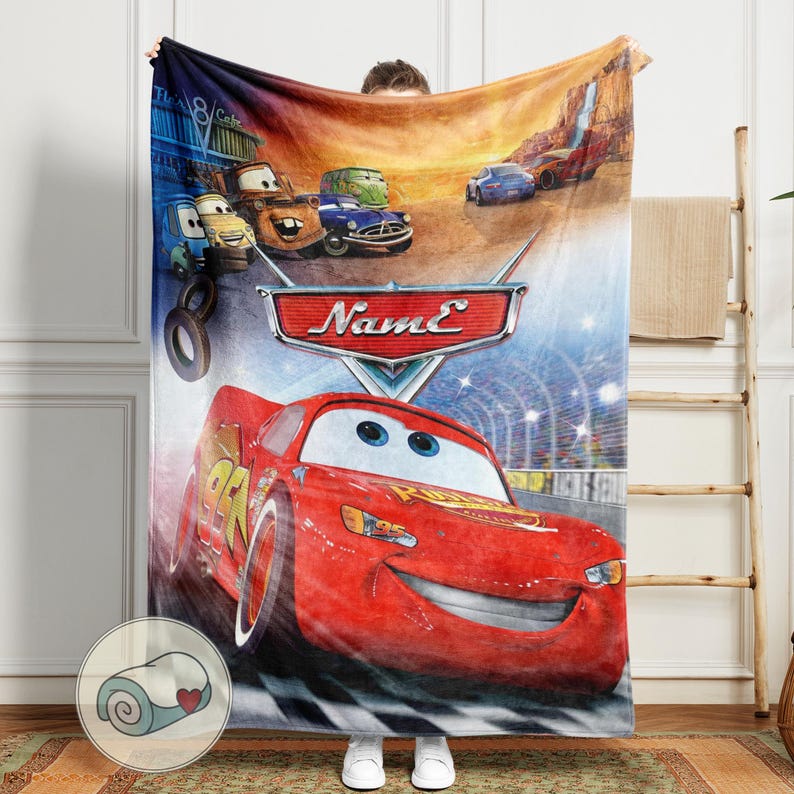 May include: A red Cars-themed blanket featuring Lightning McQueen racing on a track. The blanket showcases other characters and the text "Name" on a shield. The design includes a checkered flag pattern at the bottom.