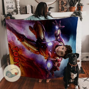 Peut inclure: Une couverture personnalis&eacute;e avec une illustration d'Iron Man et le visage d'un enfant. La couverture est principalement rouge et or, avec le nom "TONY" imprim&eacute; sur le c&ocirc;t&eacute;. Un chien noir avec un collier est assis &agrave; proximit&eacute;.