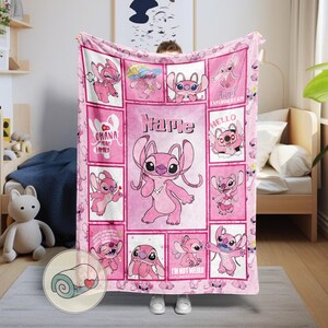 May include: Pink fleece blanket featuring the character Angel from Lilo & Stitch. The blanket has a grid design with various images of Angel, the text "Name", and other phrases. The blanket is a soft, cozy item.