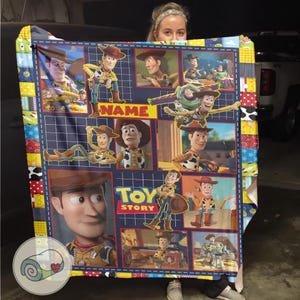 May include: A navy blue and patchwork quilt featuring images of Woody from Toy Story. The quilt has a grid design with various scenes of the character, the words "NAME" and "TOY STORY" are also visible.