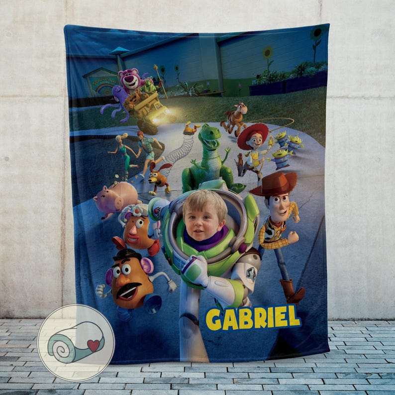 May include: A blue blanket featuring characters from the animated film "Toy Story", including Woody, Buzz Lightyear, and others. The blanket has a personalized name "GABRIEL" in yellow text. The design is set against a night sky background.