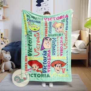 K&ouml;nnte beinhalten: Eine hellgr&uuml;ne Decke mit Cartoon-Charakteren und dem Namen "Victoria" in verschiedenen Schriftarten und Farben. Die Decke zeigt einen gr&uuml;nen Alien, ein blondes M&auml;dchen, Buzz Lightyear, ein Cowgirl und einen Cowboy.