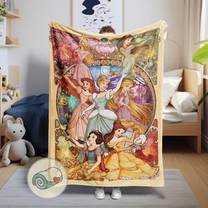 Peut inclure: Une couverture beige avec une illustration color&eacute;e de princesses Disney. Les princesses sont repr&eacute;sent&eacute;es dans leurs robes et poses embl&eacute;matiques, entour&eacute;es de bordures florales et de style art nouveau. La couverture est tenue par une personne.