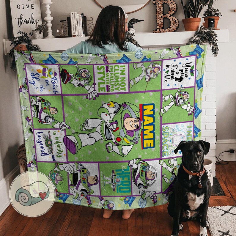 May include: A green blanket featuring Buzz Lightyear from Toy Story. The blanket has a grid design with various images of Buzz, along with phrases like "Reach for the Sky" and "To Infinity and Beyond". The word "NAME" is also visible.