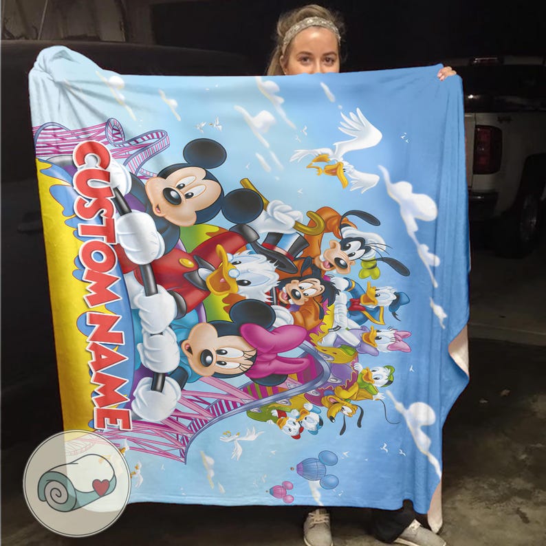May include: A blue blanket featuring Mickey Mouse and friends, with a custom name in red and white. The blanket has a cartoon design with clouds and birds, and a small image of a rolled-up blanket with a heart.