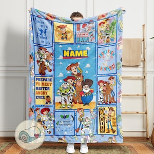May include: A light blue blanket featuring characters and quotes from the animated film series. The blanket has a central panel with the word "NAME" and several rectangular panels with character illustrations and phrases like "You've got a Friend in Me" and "To infinity and beyond!"