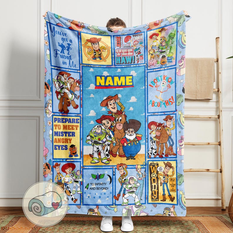 May include: A light blue blanket featuring characters and quotes from the animated film series. The blanket has a central panel with the word "NAME" and several rectangular panels with character illustrations and phrases like "You've got a Friend in Me" and "To infinity and beyond!"