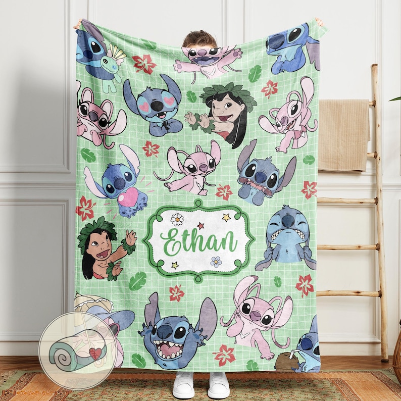 Puede incluir: Una manta verde claro con varios personajes de dibujos animados en azul y rosa, junto con detalles florales rojos y rosas. La manta tiene un patr&oacute;n de cuadr&iacute;cula y una etiqueta central con el nombre "Ethan" en verde.