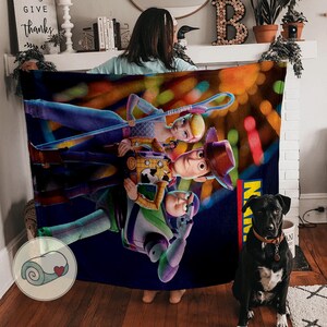 Puede incluir: Una manta de felpa con personajes de la pel&iacute;cula de animaci&oacute;n Toy Story. La manta muestra a Woody, Buzz Lightyear, Bo Peep y otros personajes sobre un fondo colorido y borroso. La manta est&aacute; sujeta por una persona.