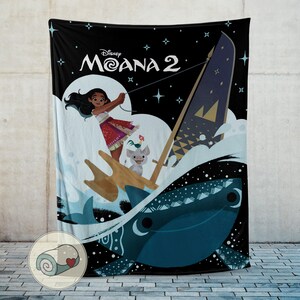 May include: Black blanket featuring a scene from Disney's Moana 2. The design includes Moana, a whale, and other characters sailing on the ocean. The blanket has a rolled-up image of the blanket in the bottom left corner.