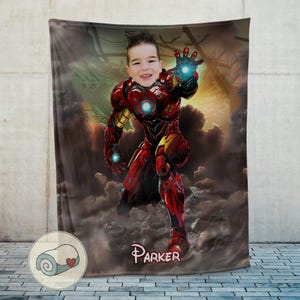 May include: A personalized blanket featuring a child's face superimposed on an Iron Man illustration. The blanket is predominantly red and gold, with a background of clouds and a cityscape. The name "Parker" is printed at the bottom.