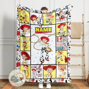 Op de afbeelding: Een wit en zwart deken met illustraties van Jessie uit Toy Story. De deken heeft een koeienprint rand en een centraal paneel met het woord "NAME". Jessie wordt afgebeeld met een lasso.